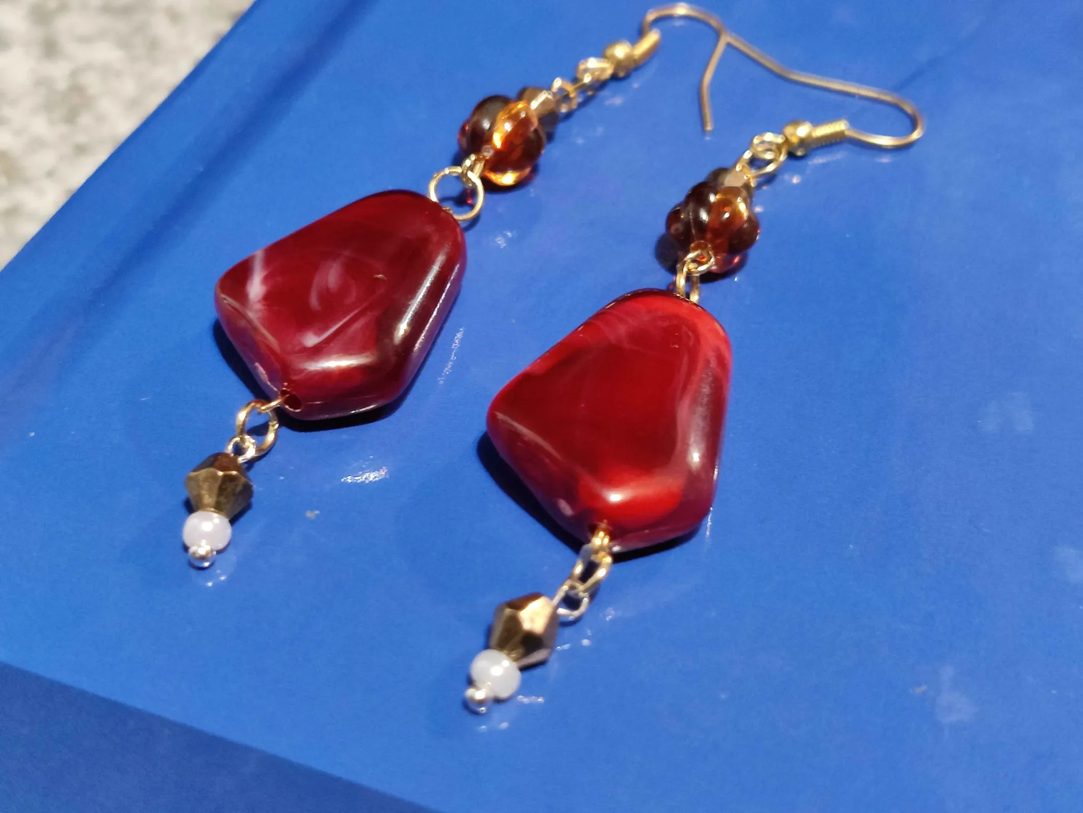 A photo of two earings featuring one large red stone with a chain below
