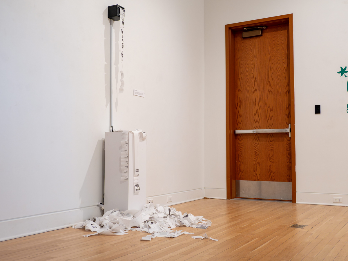 receipt printer mounted on white wall, long pile of reciept paper on the floor
